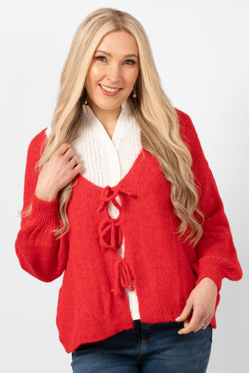 model wearing a red tie front knitted cardigan. the cardigan has long sleeves and a v-neck.