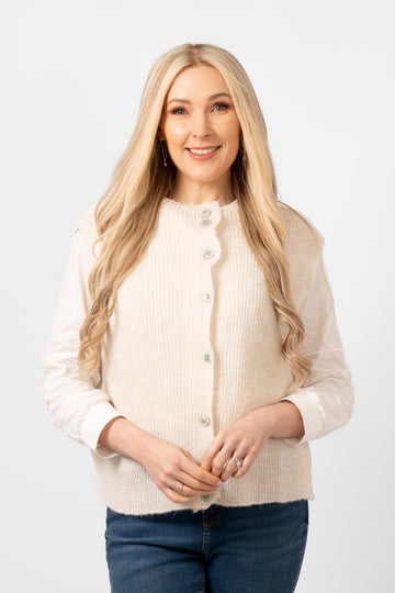 model wearing a cream coloured button front knitted tank top. the knitwear is sleeveless and has a round neck.