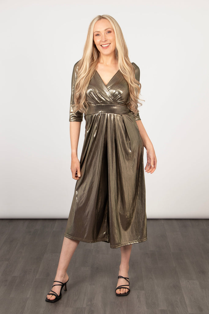 model wearing a cropped leg v-neck jumpsuit in a shiny metallic gold fabric. the jumpsuit has a shirred waist