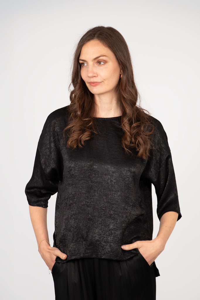 model wearing a black metallic cropped sleeve box top with a dipped hem and round neck