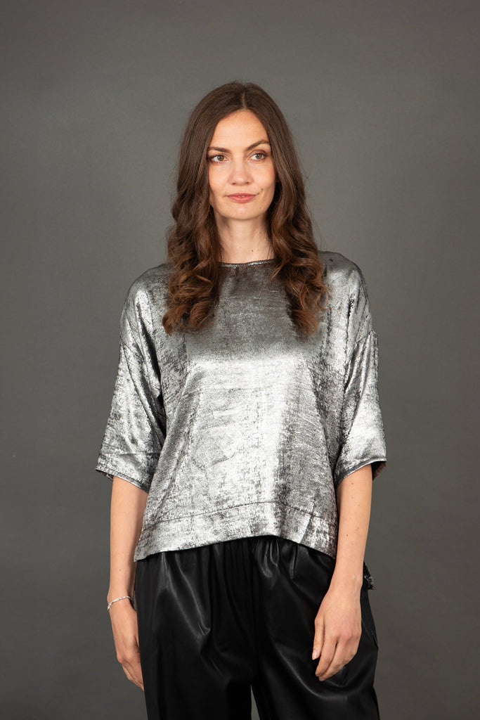 model wearing a silver box top, the sleeves sit just below the elbow and the material has an all over metallic sheen
