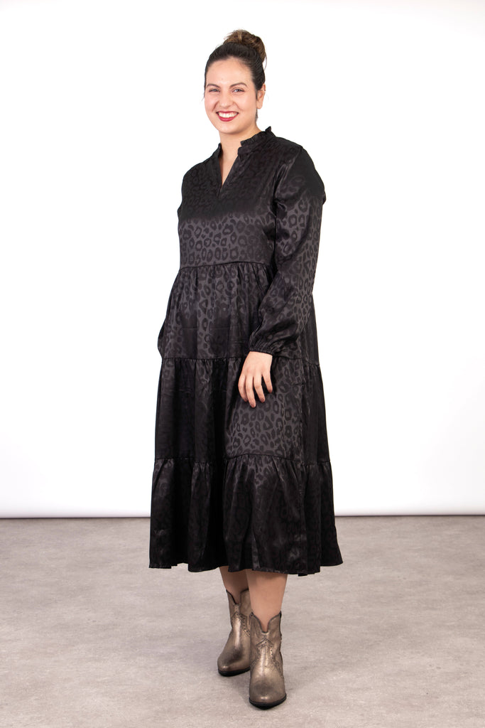 model wearing a black leopard print tiered midi dress, the dress has an open v-neck and long sleeves