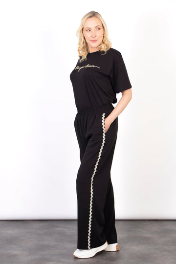 model wearing black wide leg trousers with a wavy gold glitter stripe running the full length of the leg