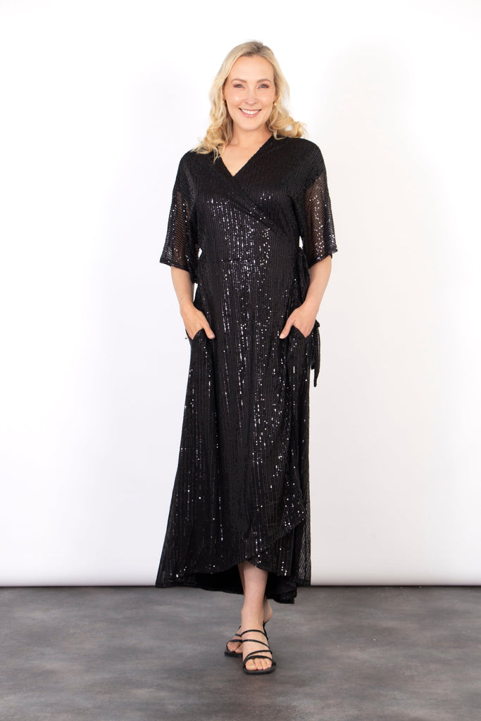 model wearing a black midi length dipped hem sparkly sequinned wrap dress with a v-neck and waist tie fastening