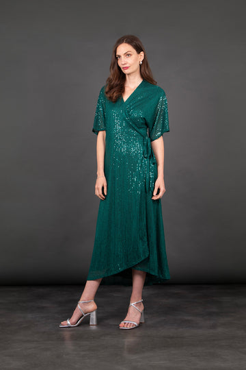 model wearing a dipped hem wrap dress in green with an all over sequin sparkle. the dress has a v-neck and waist tie