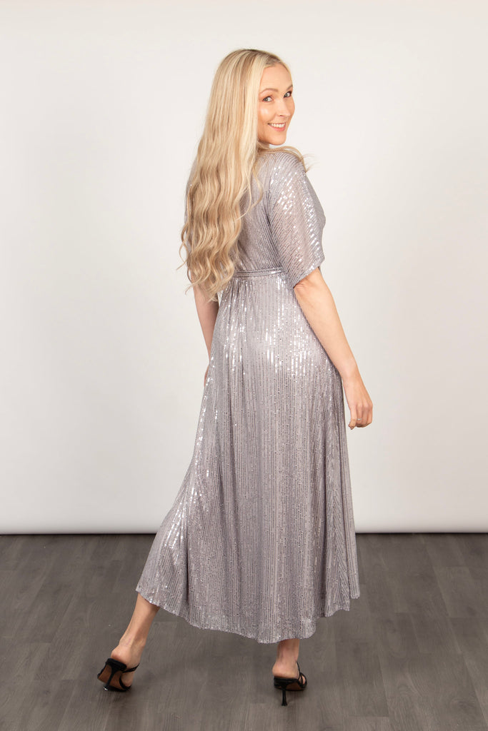 model showing the back of the silver sequin wrap dress, showing that the dress is longer at the back than at the front.