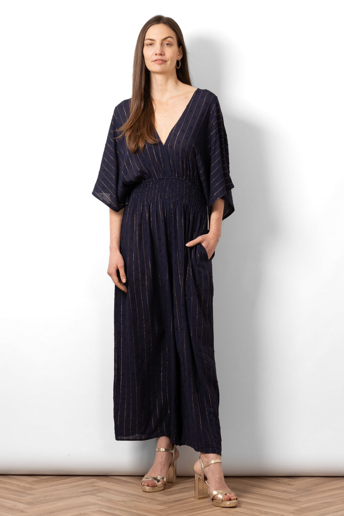 lyra-deep-v-neck-jumpsuit-navy-blue-metallic-stripe-on-model-styled-with-gold-sandals