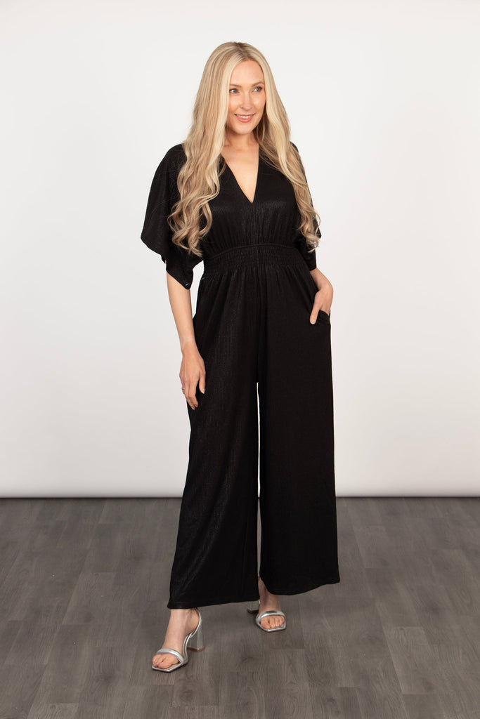 model wearing a plain black wide leg jumpsuit with angel sleeves, the jumpsuit has pockets and a wide leg design