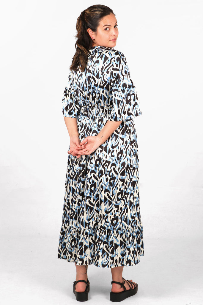 model showing the back of the blue ikat pattern maxi dress showing the shirred waist and fluted sleeves