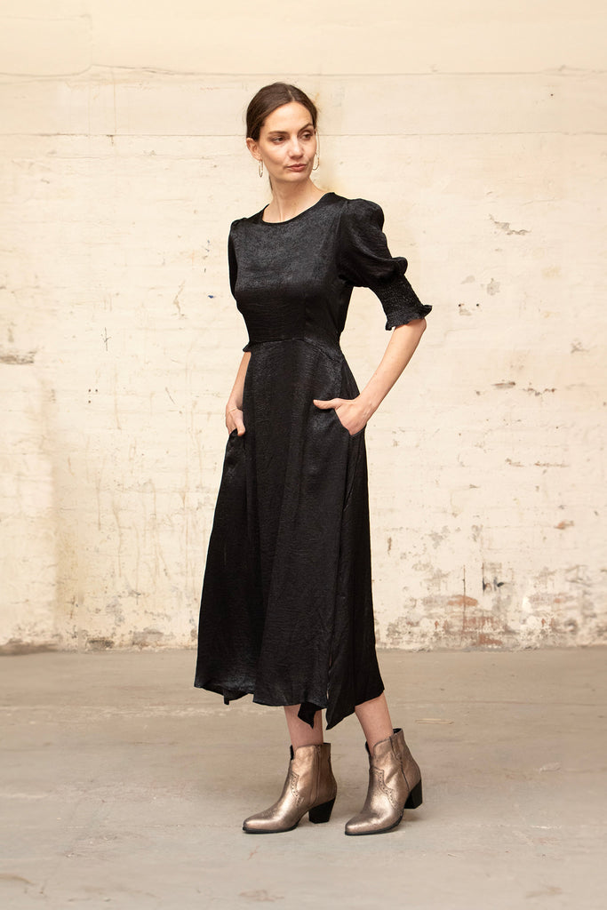 model wearing a black metallic midi tea dress with 3/4 puff sleeves and a round neck