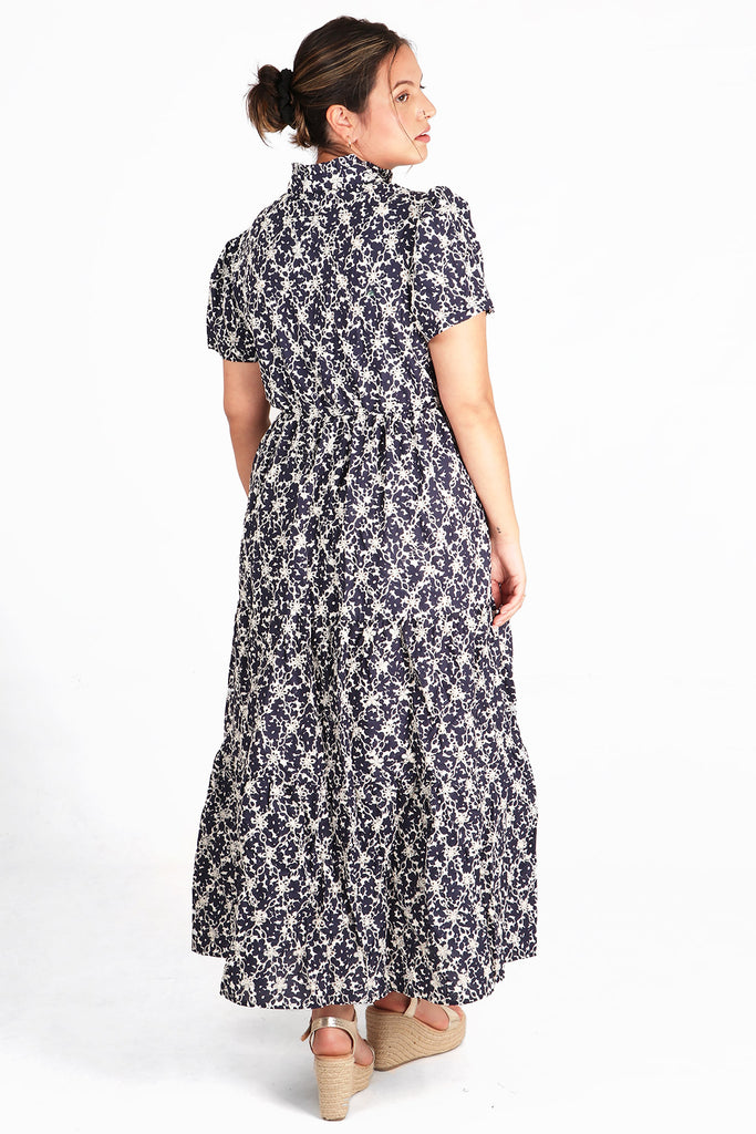 model showing the back of the tiered maxi dress showing an all over navy blue and white floral and broderie anglaise pattern
