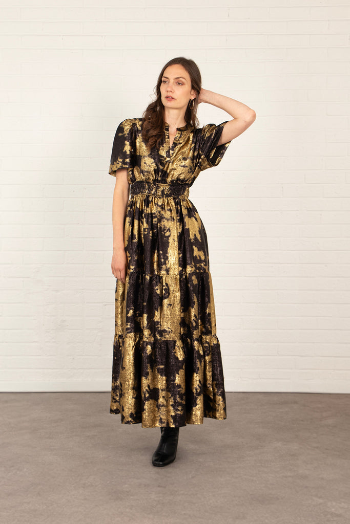 model wearing a black and gold tiered maxi dress, the dress has short sleeves and a v-neck