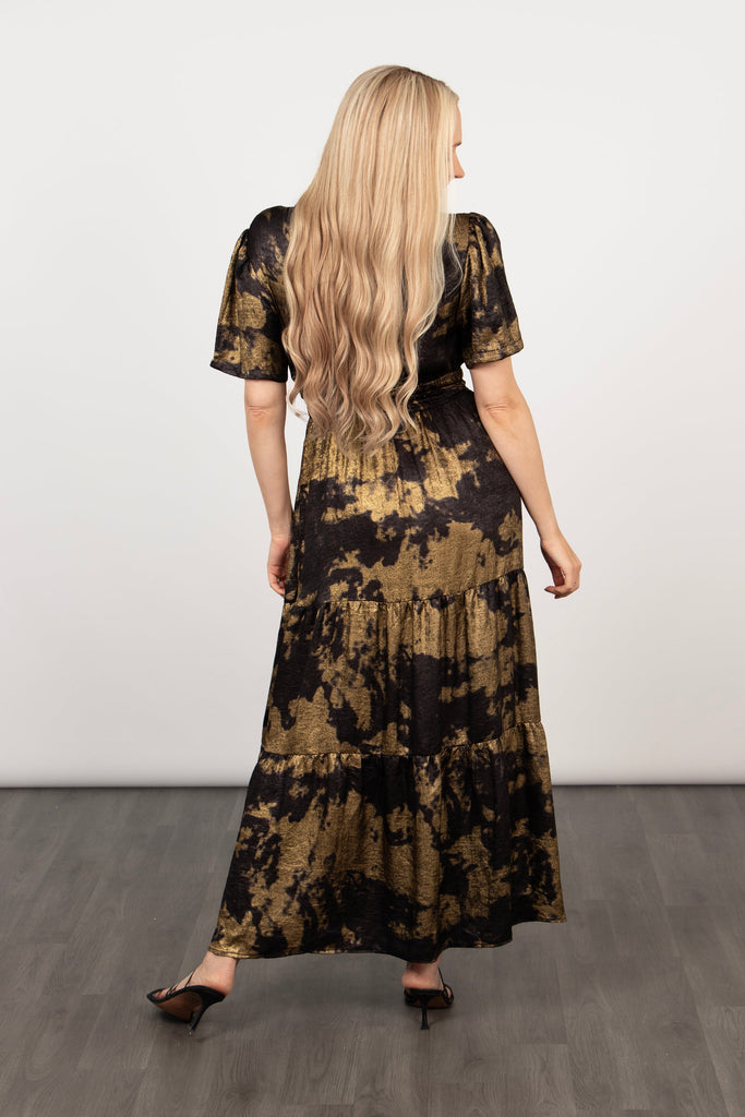 model showing the back of the tiered black and gold dress, showing the maxi length hemline