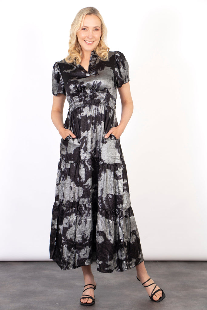 model wearing a short sleeve black and silver paint splash pattern tiered maxi dress with a metallic sheen all over. the dress has a cinched elasticated waist