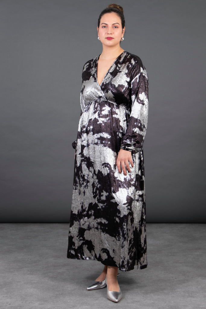 model wearing a metallic silver and grey oil slick patterned maxi dress with a faux wrap top, long sleeves and a deep v-neck