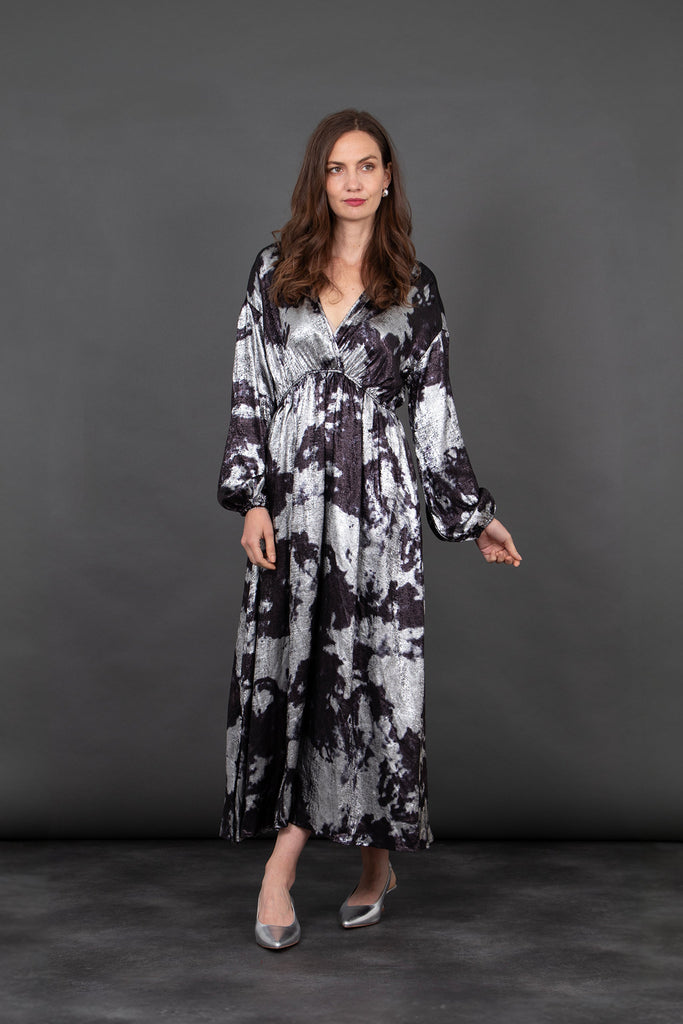 model wearing a silver and black oil slick pattern maxi dress accessorised with silver heeled shoes. the dress has long sleeves and plunging v-neck