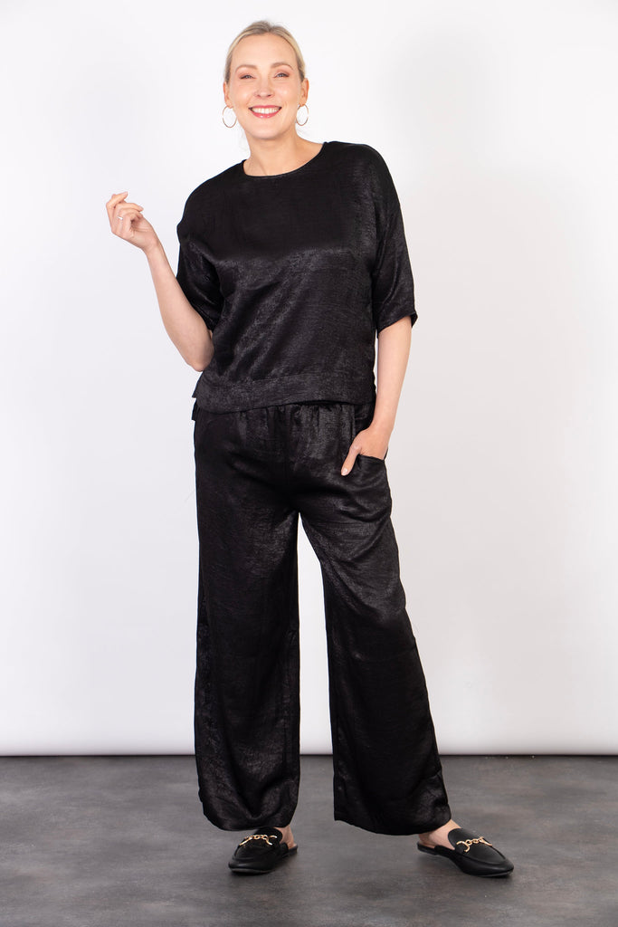 model wearing relaxed wide leg black trousers with pockets, accessorised with a matching black top and black slip on flat shoes