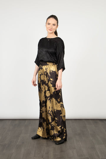 model wearing black and gold paint splash pattern wide leg trousers with a metallic sheen