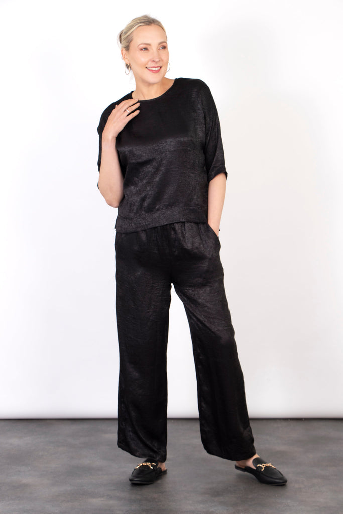 model wearing a pair of textured black metallic trousers with an elasticated shirred waist and pockets