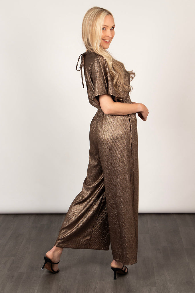model showing a side view of the bronze glitter jumpsuit, showing the wide leg design of the piece