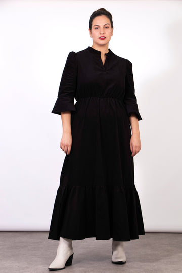 model wearing a black baby cord midaxi dress with 3/4 sleeves and a floaty tiered hem