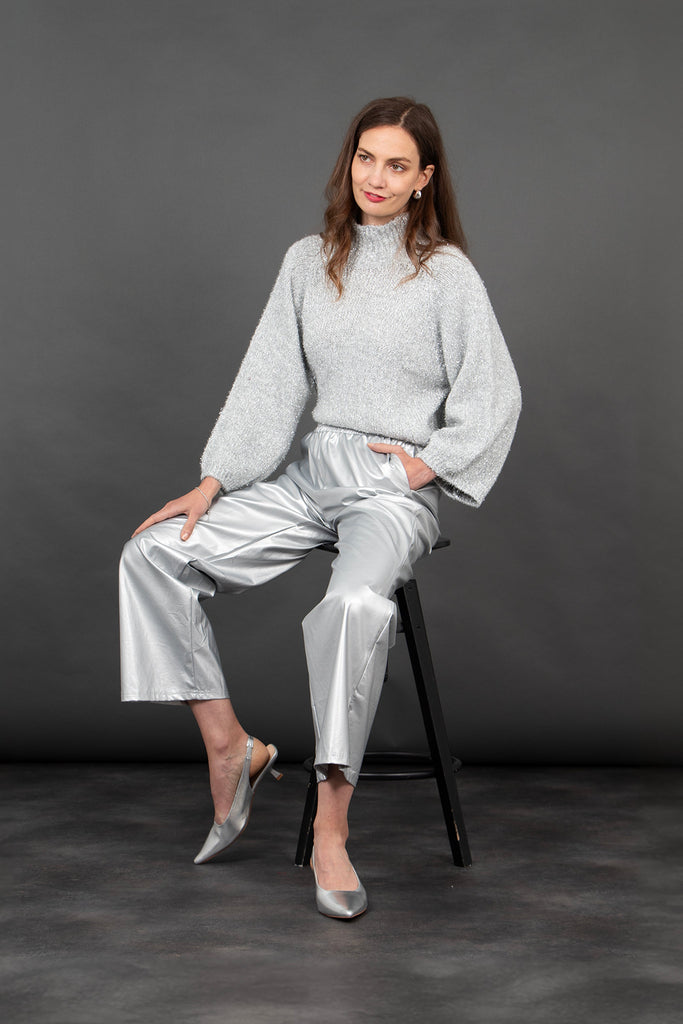 model seated wearing silver faux leather trousers accessorised with silver shoes and a sparkly silver high neck jumper