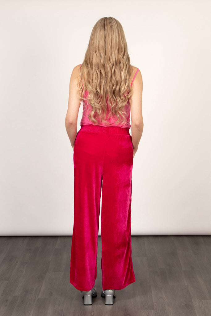 model showing the back of the fuchsia pink velvet trousers, showing the elasticated waist band and wide leg design.