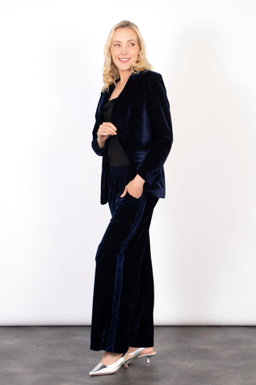 model wearing a pair of navy blue velvet trousers with a blue side stripe, the trousers are worn with a matching velvet blazer