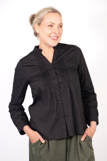 model wearing a slim fitting black cotton shirt, the shirt has pleats on the front and has button front closure