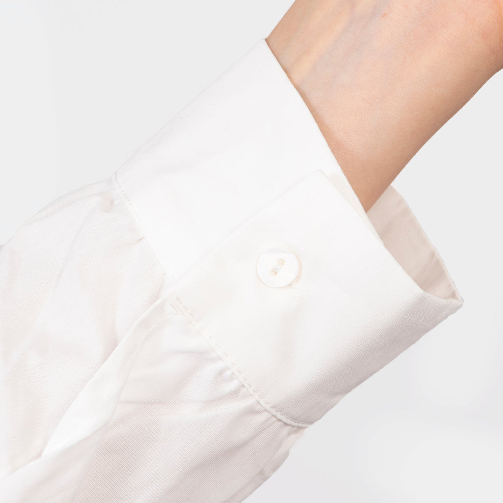 close up of the button fastening cuffs on the long sleeves of the white cotton shirt