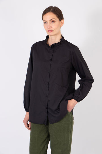 model wearing a plain black relaxed fitting cotton shirt with a frilled collar and long sleeves.