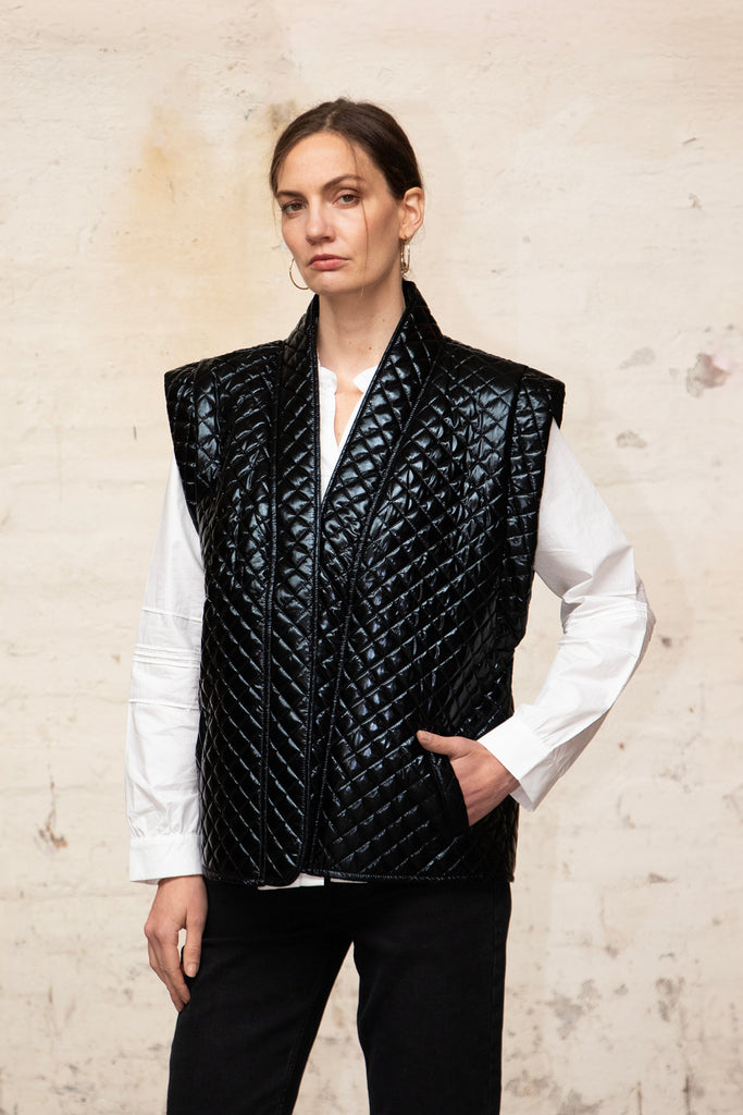 close up of the black quilted sleeveless jacket. there are pockets on the front of the design