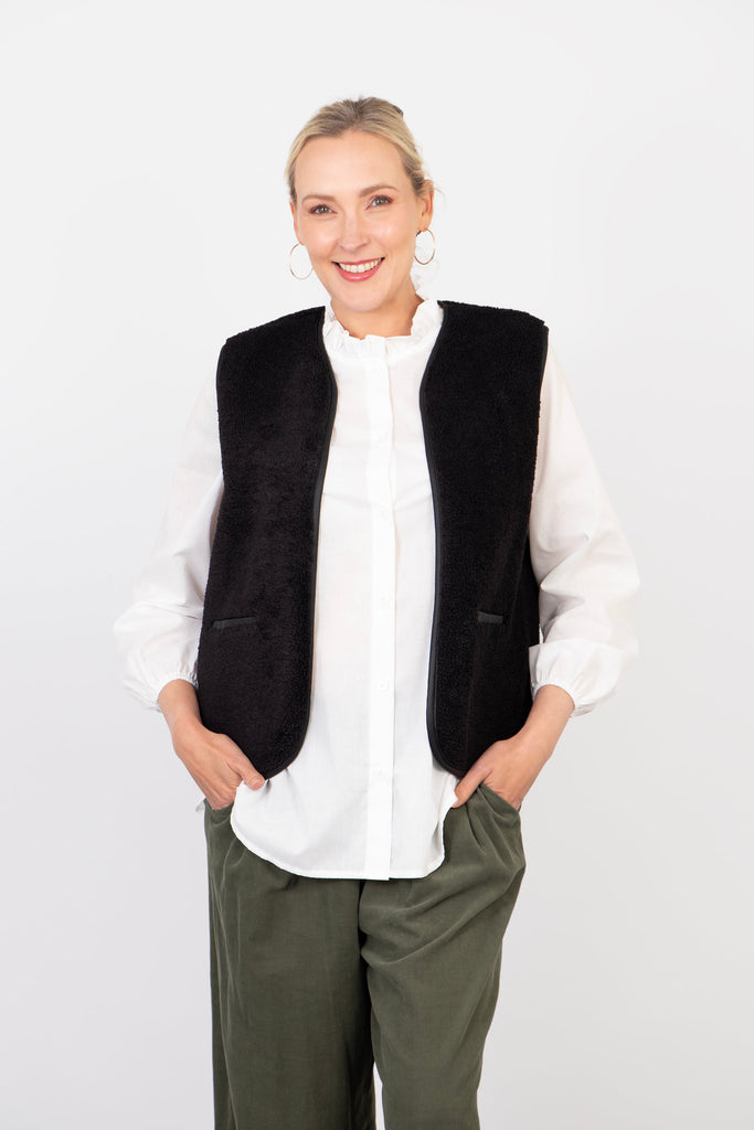 model wearing a black borg fleece vest jacket over a white shirt, showing how it would look when layered