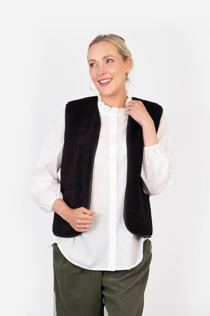 model wearing a black fleece sleeveless jacket over a white shirt