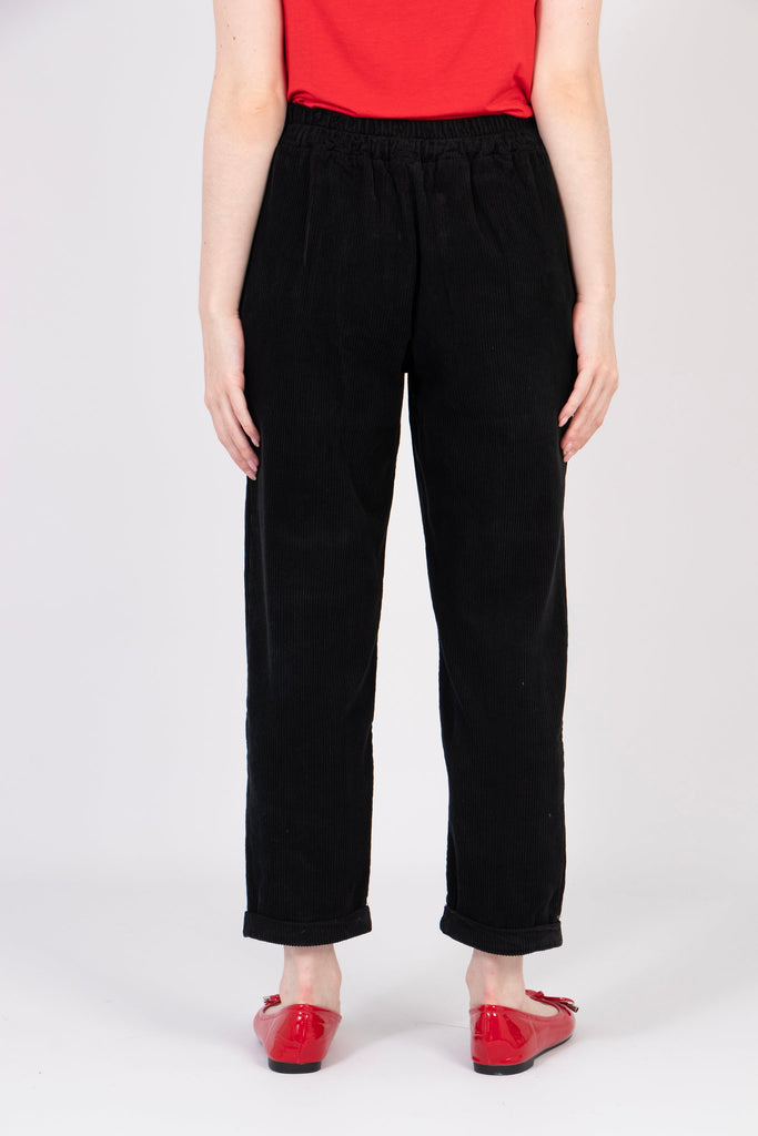 model showing the back of the black babycord trousers, the tapered leg feature is prominent, the trousers also have an elasticated waist