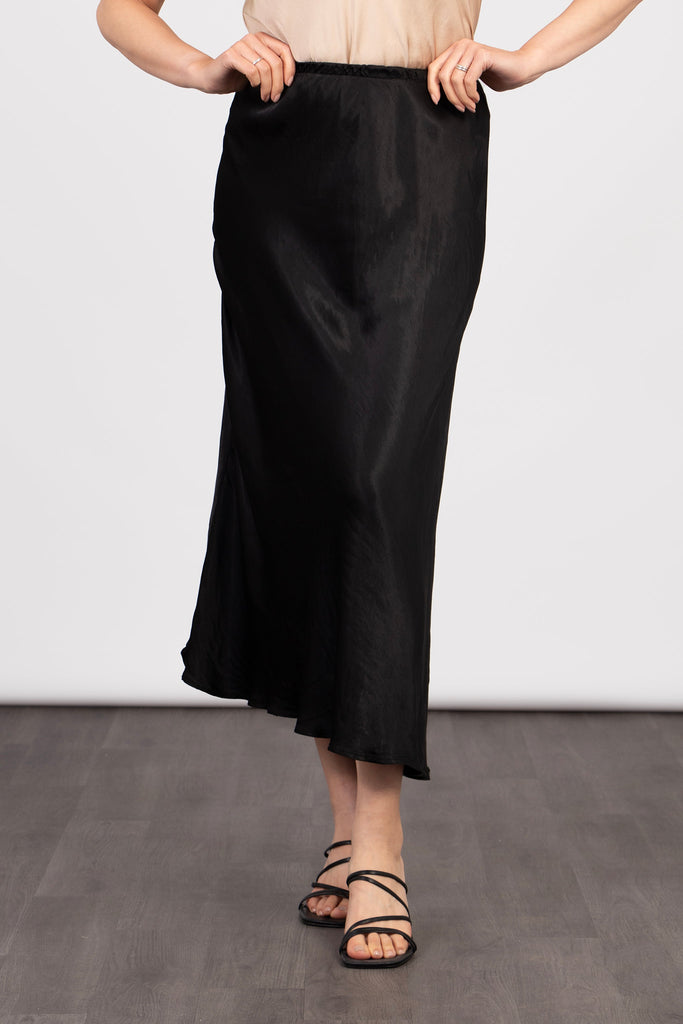 model wearing a plain black silky midi slip skirt, accessorised with a winter jumper and black shoes.