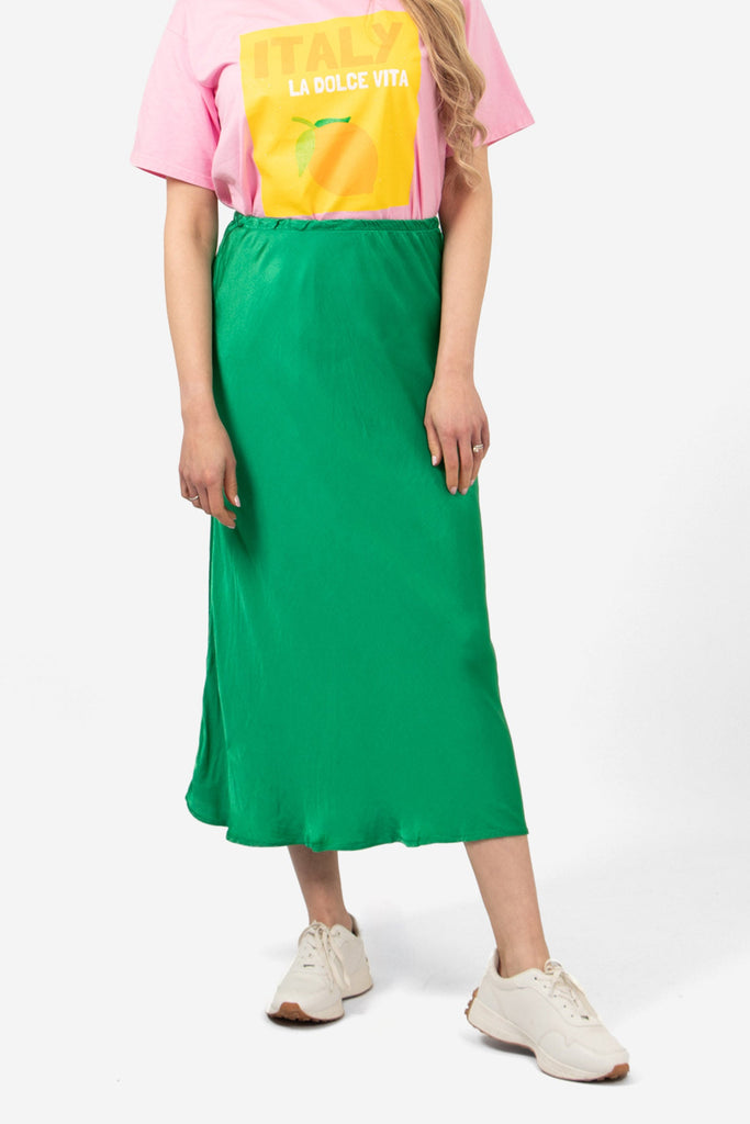 model wearing a midi length plain bright green skip skirt. the skirt has an elasticated waist and is cut on the bias