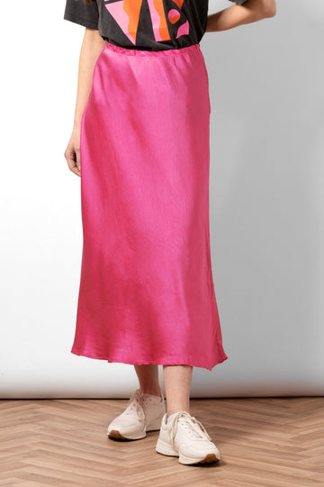 model wearing a midi length plain hot pink skip skirt. the skirt has an elasticated waist and is cut on the bias