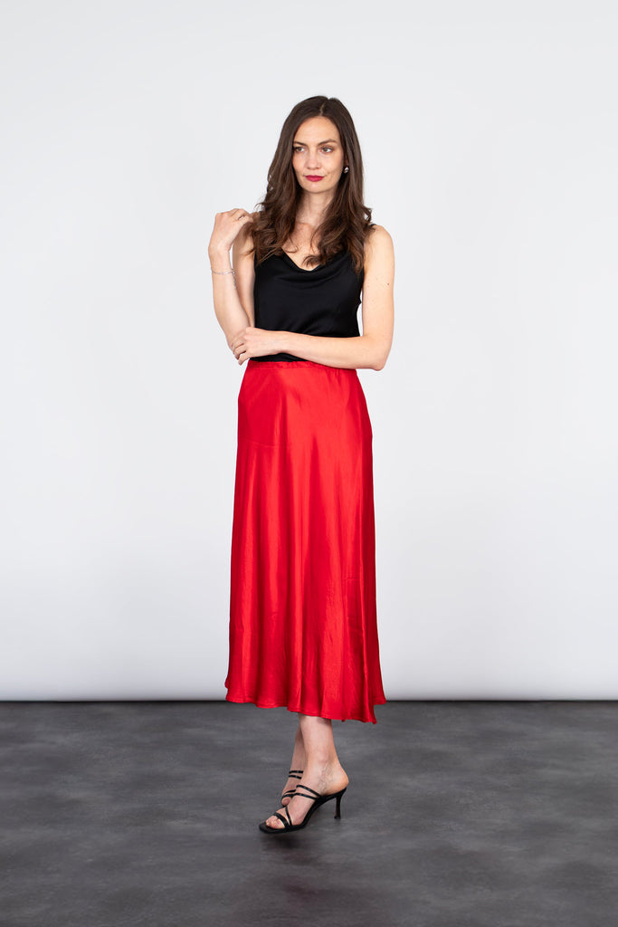 model wearing a midi length red bias cut slip skirt, accessorised with heels and a black tank top