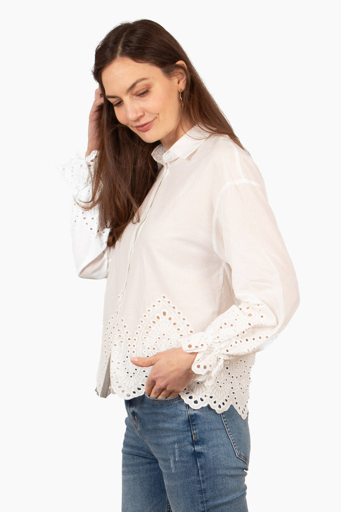side view of the white cotton shirt, showing the full length long sleeves and broderie anglaise design on the cuffs and hem. the hem of the blouse is scalloped in shape