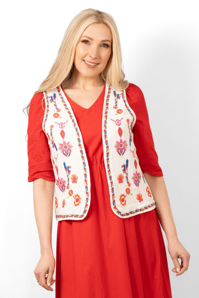 aubrey-lightweight-waistcoat-white-multi-floral-embroidery-worn-on-model-layered-over-red-dress