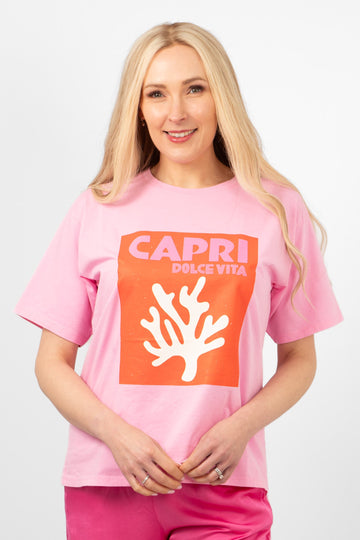 model wearing a hot pink tshirt with a coral graphic motif on the front which says capri dolce vita. the tshirt has a round neck and loose fitting short sleeves