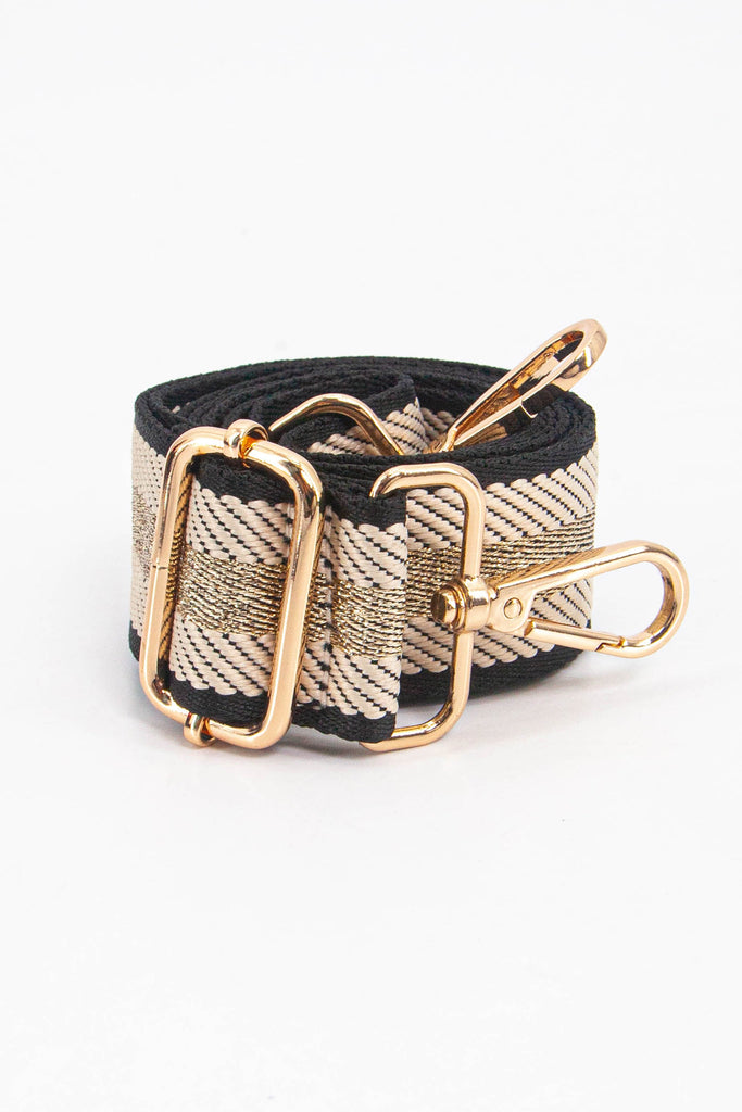 showing the bag strap coiled around itself, the cream and gold glitter stripe pattern woven design is prominent , the gold hardware is shown in close up