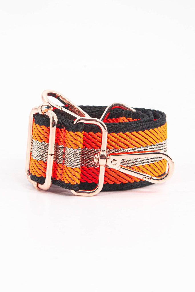 showing the bag strap coiled around itself, the orange and gold glitter stripe pattern woven design is prominent , the gold hardware is shown in close up