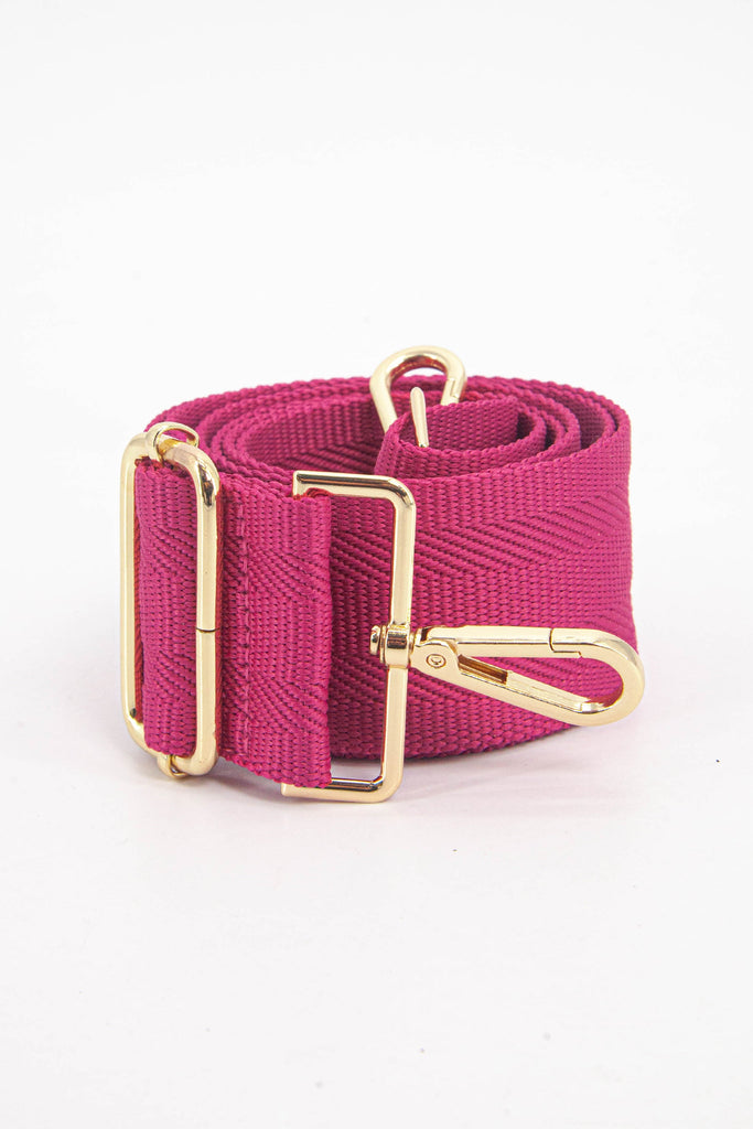 showing the bag strap coiled around itself, the woven fuchsia pink design is prominent , the gold hardware is shown in close up