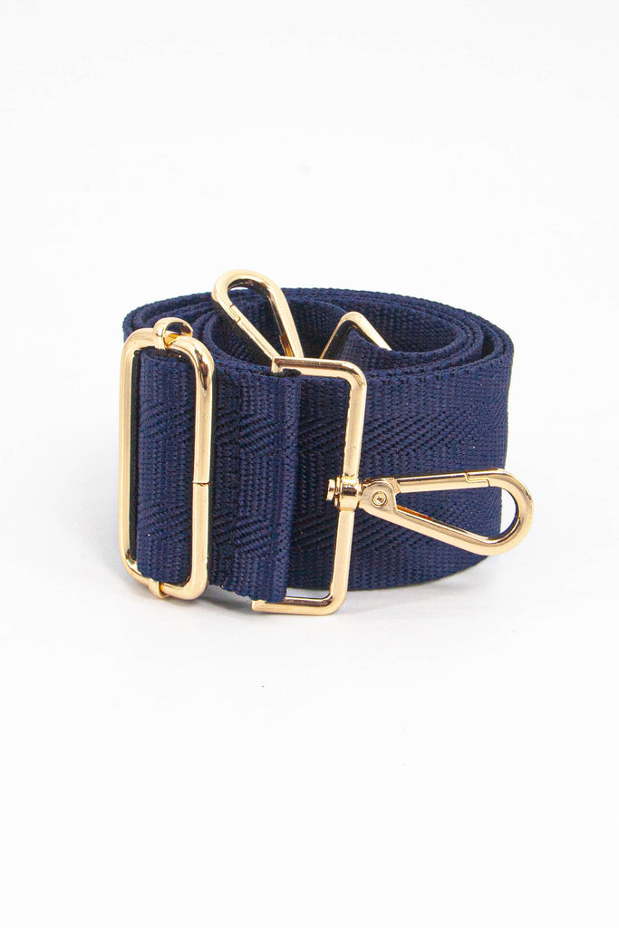 showing the bag strap coiled around itself, the woven navy blue design is prominent , the gold hardware is shown in close up