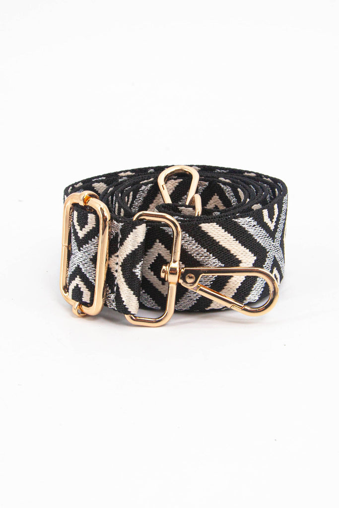 showing the bag strap coiled around itself, the grey aztec pattern woven design is prominent , the gold hardware is shown in close up