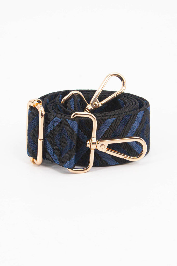 showing the bag strap coiled around itself, the blue and navy aztec pattern woven design is prominent , the gold hardware is shown in close up