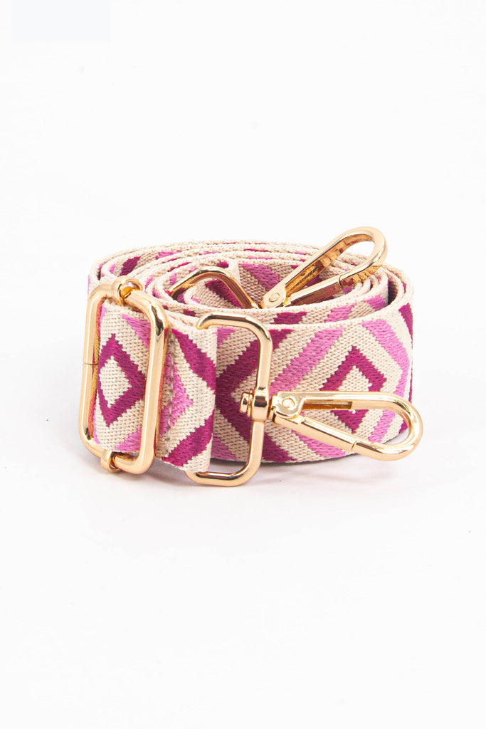 showing the bag strap coiled around itself, the pink aztec pattern woven design is prominent , the gold hardware is shown in close up