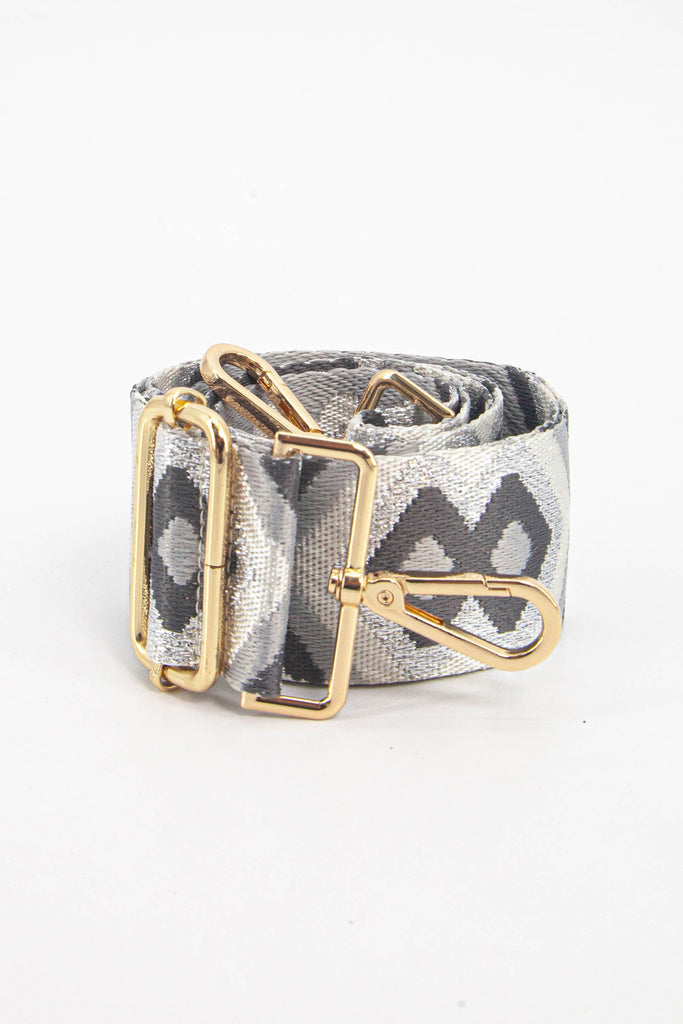 showing the bag strap coiled around itself, the grey metallic aztec pattern woven design is prominent , the gold hardware is shown in close up